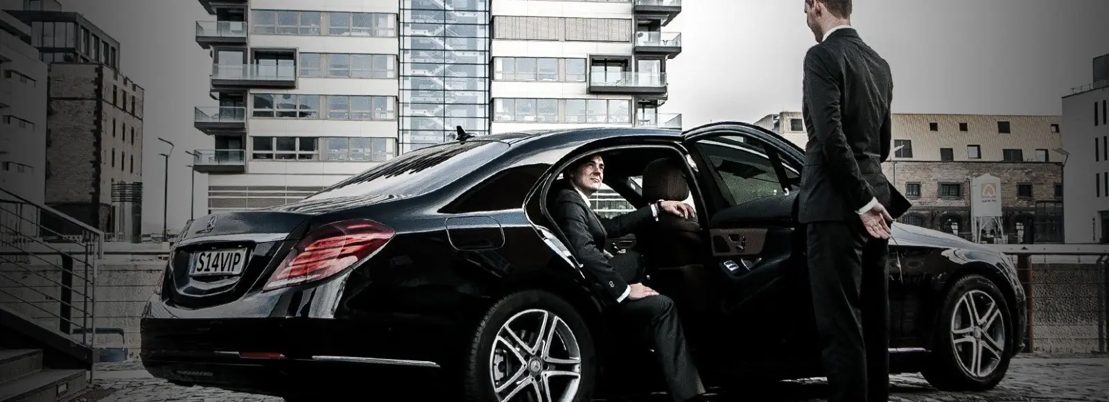 Chauffeur standing beside a black saloon taxi in Wimbledon